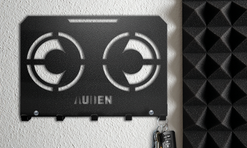 Metal wall key holder with a geometric cutout design and personalized name, mounted on a textured wall.