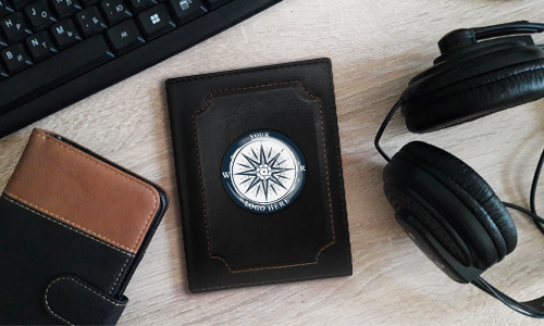 Flat lay with leather-bound items: black keyboard, headphones, brown notebook, and black journal with compass design