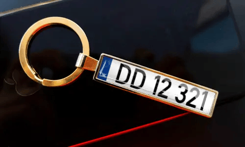 License plate keychain attached to keys in pocket with car in background