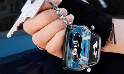 Hand die een sleutelhanger in de vorm van een blauwe auto vasthoudt met een gedetailleerd frontontwerp