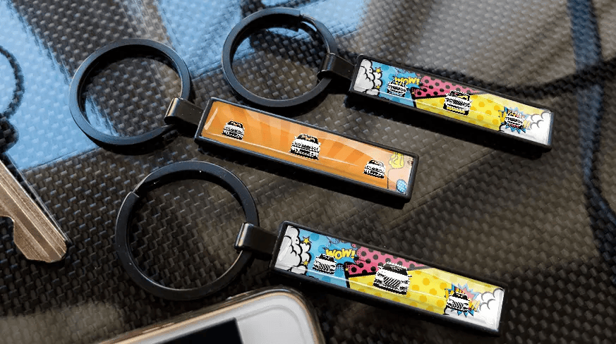 Comic-style license plate keychains with colorful car designs displayed on a carbon-textured surface
